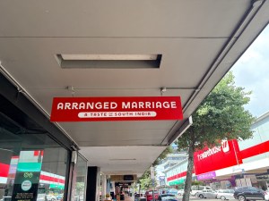 Sign for 'Arranged Marriage' restaurant, featuring the tagline 'A Taste of South India', hanging above a street.